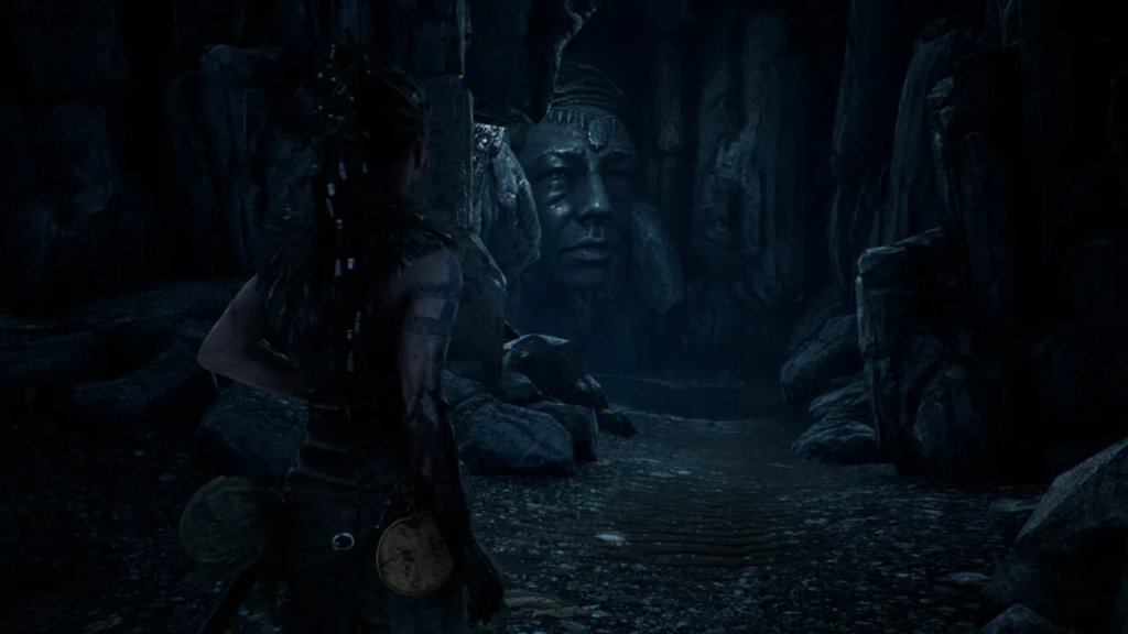 Сенуа из Hellblade стоит в пещере у лица-скалы